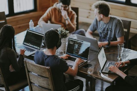 Een team ontwikkelaars werkt samen aan laptops aan een houten tafel.